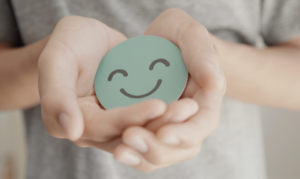 Put your mental health first image with two hands holding a smiley face sticker facing toward you.