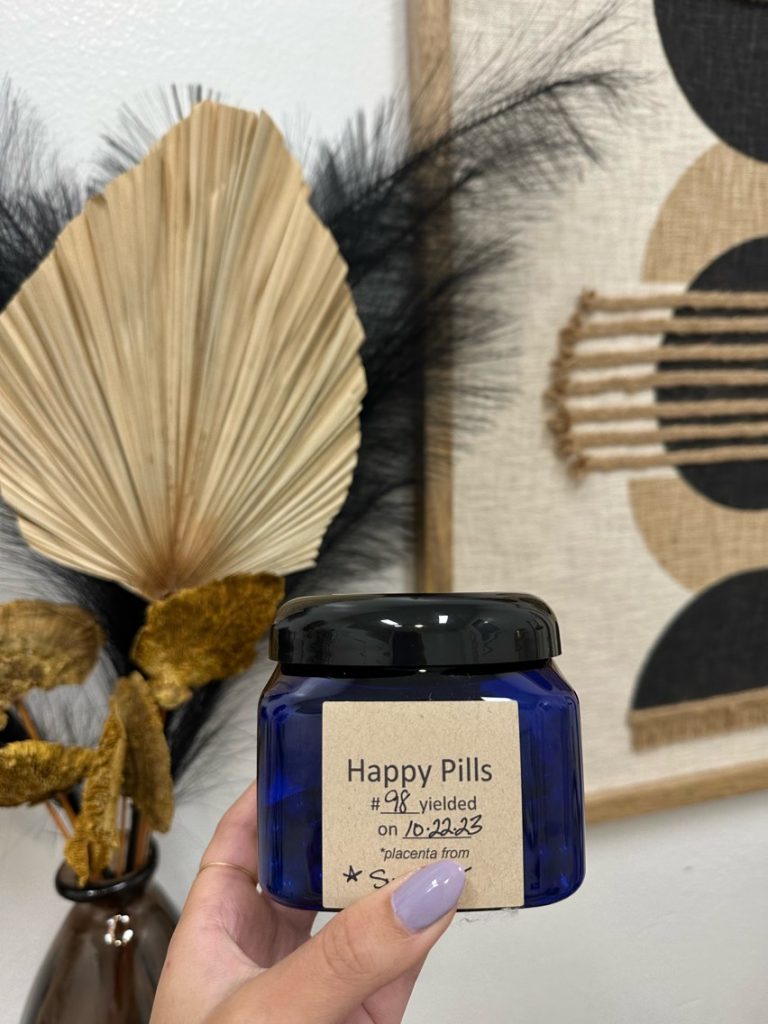 a hand holding a blue container labeled Happy Pills which is the container the placenta pills are in